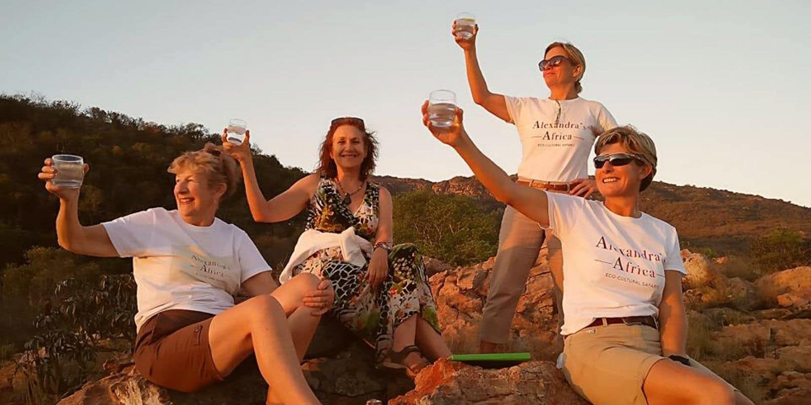 Image of Alexandra's Africa Team - 4 women sitting on rocks raising a glass to the setting sun