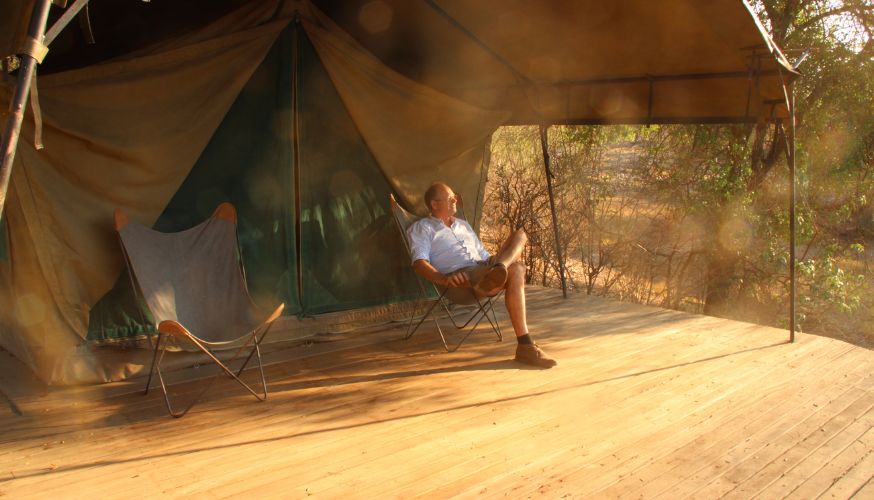 Man sitting and relaxing on the patio decking outside his tent overlooking the Limpopo River