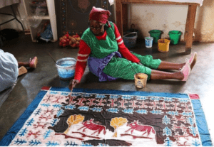 An African lady from the co-operative Twananani Textiles seated on the floor of the workshop finishing off a batik, table cloth design