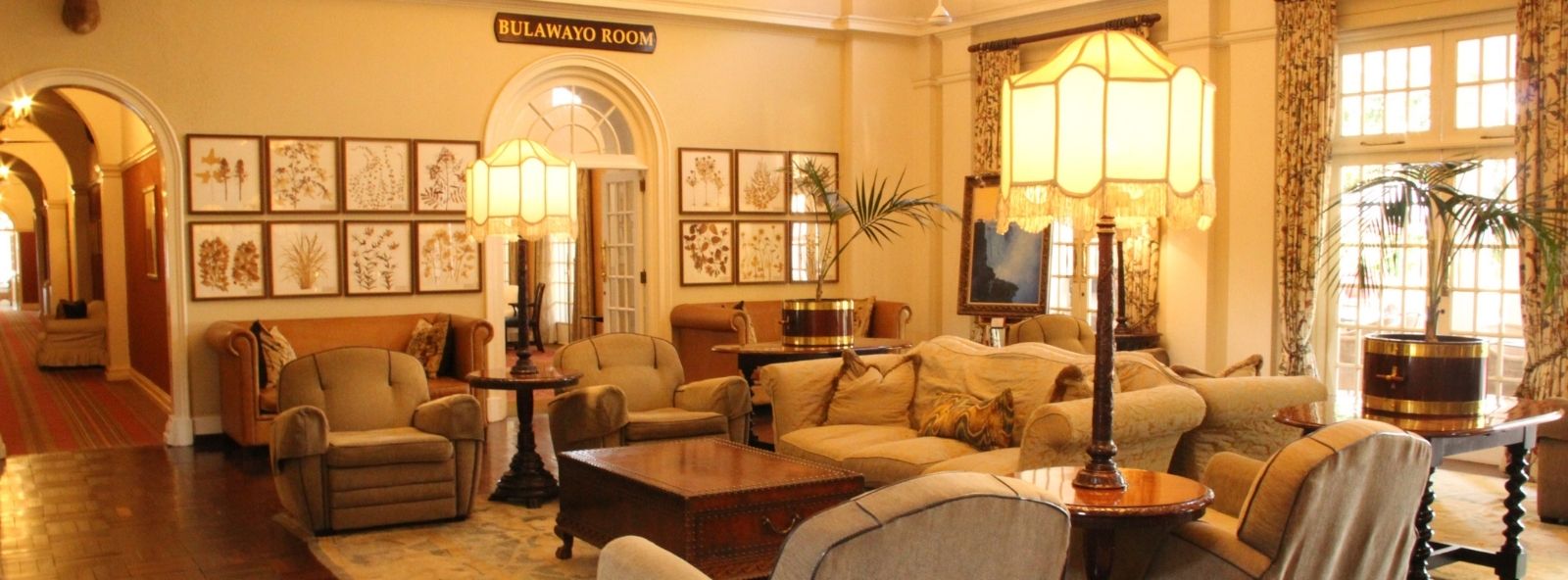 Enjoy the splendour of a bygone era. Anyone for tea? The magnificent sitting room of the Victoria Falls Hotel - A room tastefully furnished with armchairs, lamps, piano and polished side tables and plants - colonial style