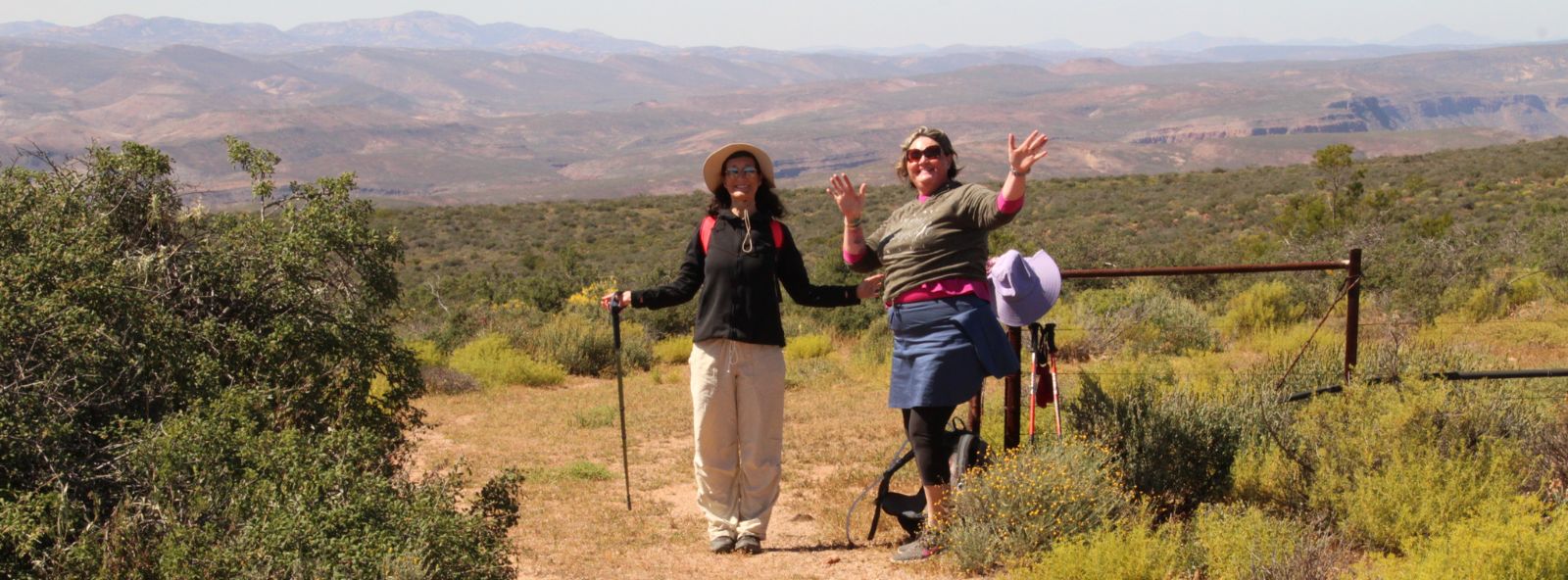 Two women facing the camera and waving in hiking clothes with Schaap River Canyon in Background