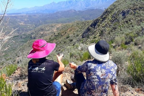 Two women in sun hats sitting on top of mountain looking out over valley below